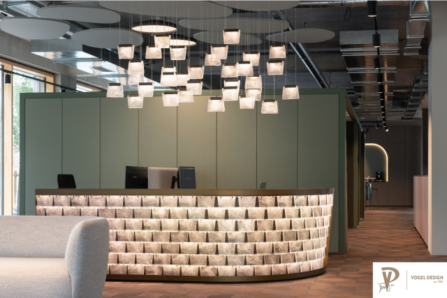 Empfangstresen mit Glaselementen und einer Glasleuchte von der Decke hängend. Im Hintergrund steht ein olivfarbiger Schrank als Raumtrennung, rechts verläuft ein Gang nach hinten.